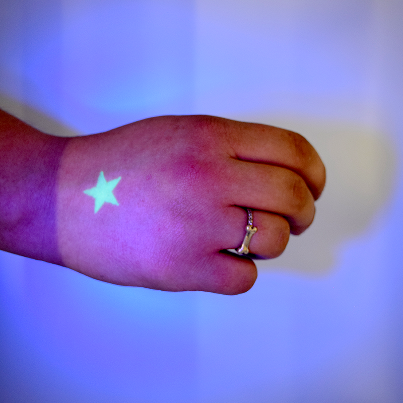 picture of a hand stamped with a star in glowing UV ink